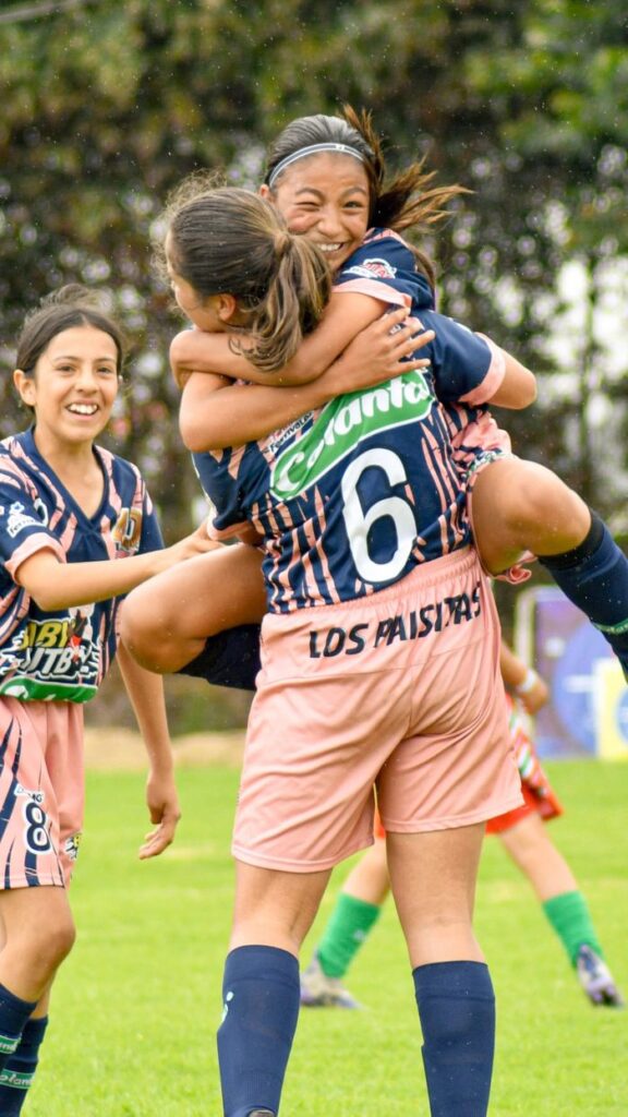 Teenage girls celebrate their soccer match victory with joyful hugs on the field.