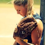 A teenage girl holds a softball glove while looking downward very depressed