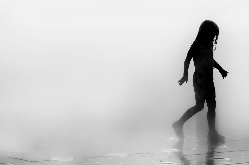 Artistic black and white silhouette of a child playing in foggy mist.