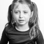 Black and white young girl with hair up in casual clothes crying against white background