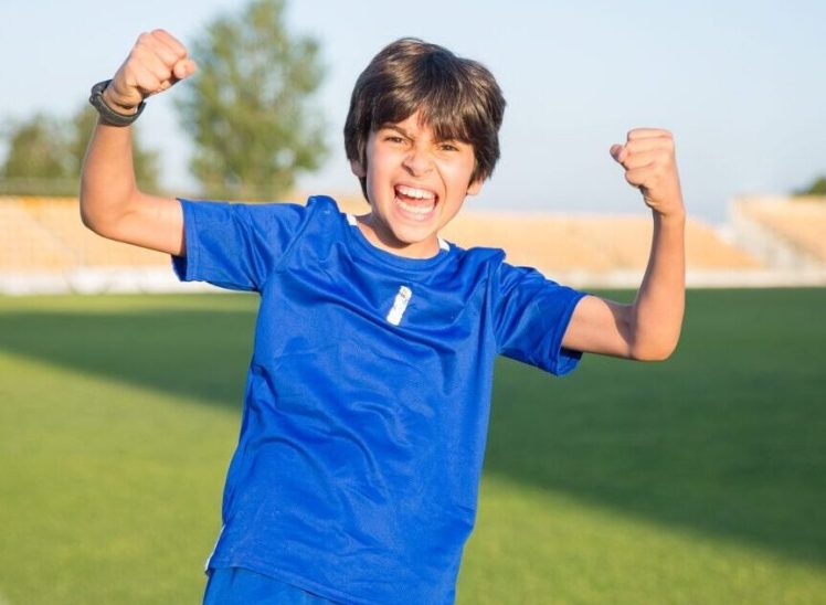 Joyful boy with arms flexed celebrating a soccer win outdoors